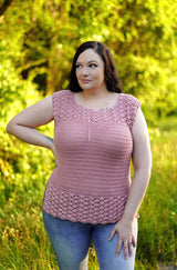 Front view of pale pink crochet top on a woman wearing jeans, standing in front of tall grass and green trees. The top has textured bands at the top and bottom, with a plain torso.  thumbnail
