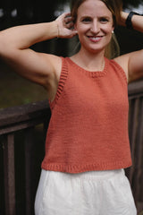 Woman has her arms up to hold back long hair. She wears a rust colored knit tank top with ribbed armholes, neck, and hem.  thumbnail