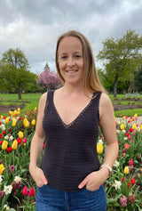 Woman in a black crochet tank top and jeans stands in front of a bed of tulips in bloom. A cherry tree is visible in the background.  thumbnail