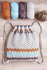 Flat lay photo of crochet drawstring backpack. The body of the bag is beige, with stripes of brown, pale blue, and amber gold at top and bottom. There are 4 yarn balls and a decorative rope knot ball at top of frame.  thumbnail