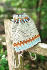 Crochet backpack sitting on top rail of split wood fence.  thumbnail