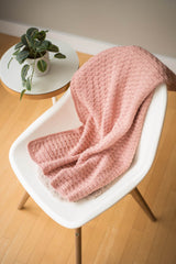 Pink baby blanket is draped over a white chair, with a potted plant on a side table nearby.  thumbnail