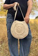 Cropped front view of woman in black t-shirt and cargo pants standing in a field of tall grass. She holds a circle crochet bag with a long strap.  thumbnail
