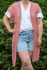 Cropped front view of a woman in a white button up and jean shorts wearing a long crochet sleeveless cardigan.  thumbnail