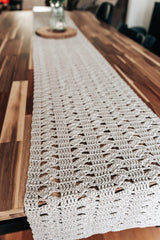 End of table runner showing columns of solid and alternating shells. The runner is made in a pale greige color, laid on a wooden table. There is a wooden coaster with a vase of flowers in the background.  thumbnail