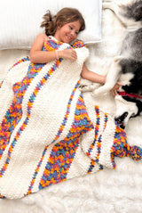 Young girl cuddles under crochet blanket with a husky dog. The blanket is white and multi-colored in stripes.  thumbnail