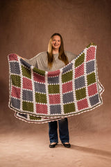 Woman standing in front of studio background holding crochet afghan folded in half.  thumbnail