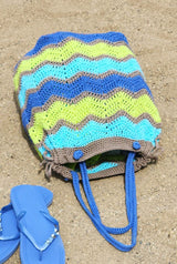 Crochet ripple bag laid flat on beach, with blue flip flops nearby.  thumbnail
