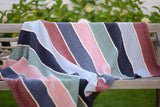 Full view of striped knit blanket draped over park bench. It is knot in stockinette stitch with ribbed borders.  thumbnail
