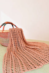 Crochet lacy blanket in a faded clay color spills out of a woven blanket.  thumbnail