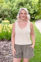 Full view of woman wearing cream knit tank and khaki shorts, in front of a flower bed with yellow blooms and wood mulch.  thumbnail