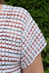 Close up of shoulder and sleeve on crochet top. It is made of blocks in white with narrow stripes of russet, mauve, and sky blue.  thumbnail