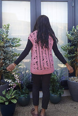 Back view of crochet vest, in a mauve-pink color. The vest has an open lace stitch pattern running vertically, and ribbing on the bottom.  thumbnail
