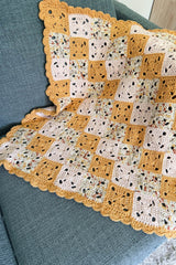 Top down view of baby blanket made of small granny squares seamed together. The blanket has a scalloped border all the way around.  thumbnail