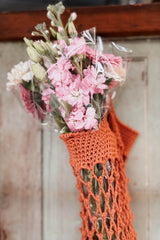 Close up of top of crochet market bag, showing solid top edge and mesh body. The bag is a golden brown color, and there is a bouquet of pink flowers in the bag.  thumbnail