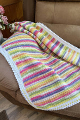 Colorful crochet baby blanket draped over brown armchair. The body of the blanket is striped in purple, pink, white, green, and yellow. It has a lacy white border.  thumbnail