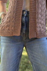 Close up of lower hem of knit lace cardigan, showing ribbed bottom and front bands. The cardigan is a soft brown color, worn with a white t-shirt and jeans.  thumbnail