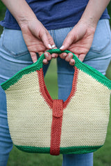 Woman holds crochet purse behind her with both hands in top handle.  thumbnail