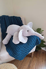 Crochet elephant sits on a blue afghan on a grey chair.  thumbnail