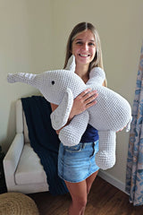 Teenager holds a stuffed crochet elephant, with floppy legs and a short tail.  thumbnail