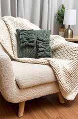 Sage green pillow with ruffle detail sits on a cream knit throw on a cream armchair.  thumbnail