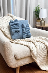 Sky blue knit pillow on a cream knit throw on a cream armchair.  thumbnail