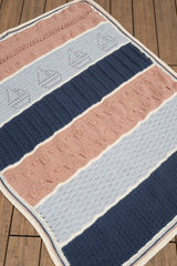 Striped crochet afghan laid on wooden floor. The afghan has sections of navy blue, light blue, and pale orange separated by cream. Each section is a different texture.  thumbnail