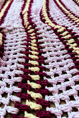 Close up of texture in crochet afghan, showing open puff stitch pattern combined with stripes of ale purple, dark wine purple, and cream.  thumbnail