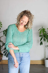 Front view of woman wearing crochet top with jeans, pushing up her right sleeve. The pullover has a scoop neck, a lace body, and solid hem & sides.  thumbnail