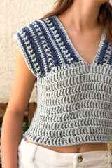 Cropped close up of crochet top on a woman, wearing white jeans. The top has a solid pale blue body and wide shoulder straps striped in pale and dark blue.  thumbnail