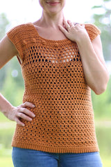 Cropped front view of woman in a golden orange crochet top and jeans, standing outdoors. The top has a mesh panel across the upper bust with a row of bobbles above. The shoulders and body are worked in different stitch patterns.  thumbnail