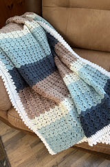 Crochet baby blanket draped over brown armchair.  thumbnail