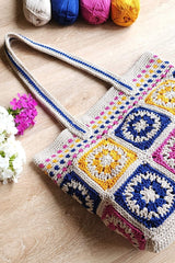Side angle view of crochet tote bag. Bag is made of granny squares in a linen color paired with either blue, pink, or yellow. The top band of the bag has those colors in dashed stripes. The handles are linen and blue and long enough to go over the shoulder.  thumbnail