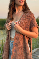 Cropped side view of woman wearing open crochet cardigan with split sides. The cardigan has scattered bobbles and rows of mesh, and is photographed at golden hour.  thumbnail
