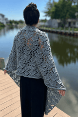 Back view of woman in a black dress standing on a dock looking over a canal. She wears a knitted lacy shawl in a pale blue.  thumbnail