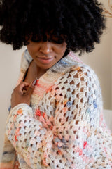 Side view of top shoulder, showing granny stitch pattern, drop shoulder, and ribbed front band. The yarn is a white base with flecks of orange, brown, blue, and red.  thumbnail