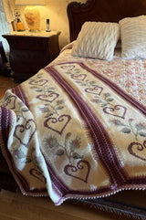 Crochet afghan with embroidered red hearts and borders draped over corner of bed.  thumbnail