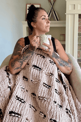 Woman snuggled under blanket, holding coffee cup and looking right.  thumbnail