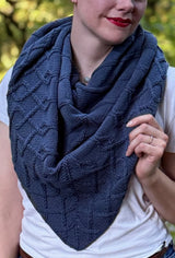 Cropped front view of triangular knit shawl worn bandana style over a white t-shirt. The shawl is a deep teal blue and has an all-over cable design.  thumbnail