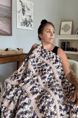 Woman sitting under crochet blanket in armchair, looking right.  thumbnail
