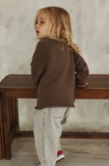 Back view of toddler leaning on bench, wearing a brown raglan sweater with commercial-style shaping.  thumbnail