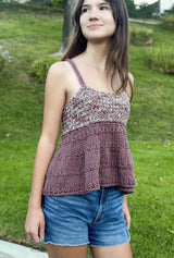 Young woman in a knit tank top and denim shorts, standing in front of a grassy hill. The tank top has a marled bodice and a mauve lower body with a-line shaping.  thumbnail