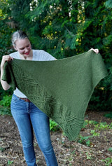 Woman holds triangular knit shawl out to the side, standing outdoors. The shawl has a wide cable panel up one side and a garter stitch body.  thumbnail