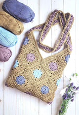 Flat lay of rectangular bag with crossbody strap, laid on white wooden surface. The bag is made in tan with flowers in periwinkle, pale mauve, and icy blue.  thumbnail