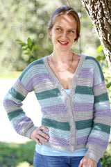 Woman in a striped crochet cardigan stands near a tree in a green backyard.  thumbnail