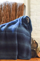 Crocheted throw in shades of blue craped over armchair, with a stack of firewood nearby. thumbnail