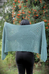 Back view of woman holding up rectangular shawl, showing diagonal lines of eyelets. The shawl is a sagey green.  thumbnail