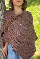 Front view of a crochet poncho worn by a young girl, with jeans, standing in front of a tree in a green backyard.  thumbnail