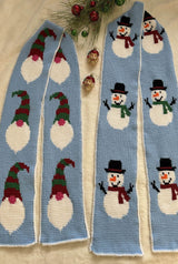 Two Tunisian crochet scarves laid on a white tablecloth. The scarves are pale blue with white borders. One has gnome-style Santas and one has snowmen.  thumbnail
