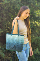 Woman standing outside in front of evergreen tree holding tote bag up to her shoulder.  thumbnail